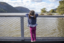 Little girl standing on a fence in front of water