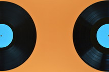 two old black vinyl records with blank cyan labels on orange background