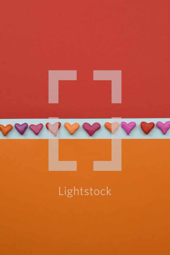hearts in a row as ribon on white between orange and red paper with copy space above and below as sign for love and relationship or emotions