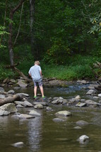 a boy standing in shallow water of a river 