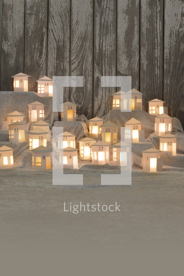 Advent calendar out of 24 self small made white round paper houses illuminated from the inside on white satin for Advent with copy space below
