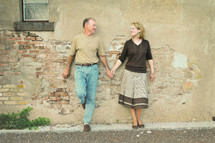 Couple holding hands while standing against an adobe house.