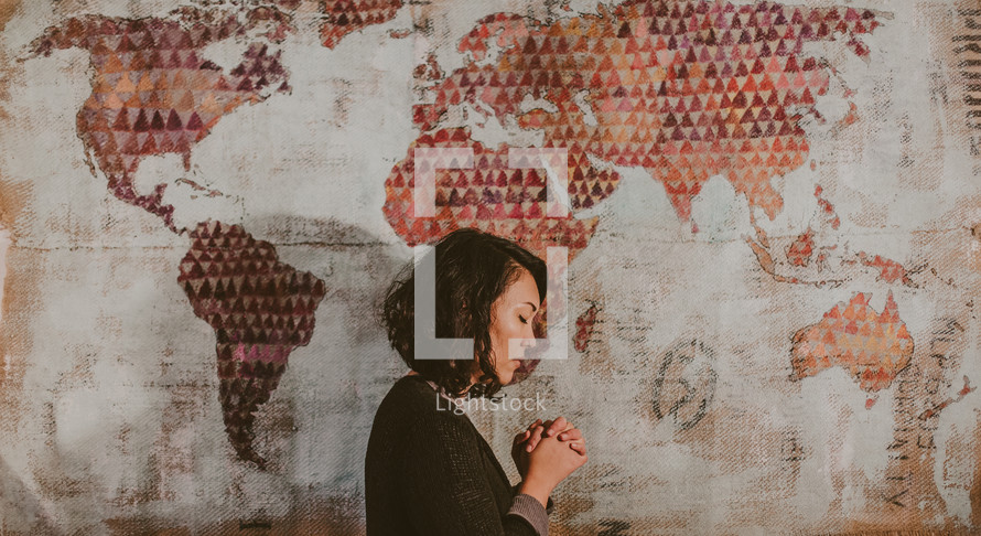 A woman praying in front of a world map 