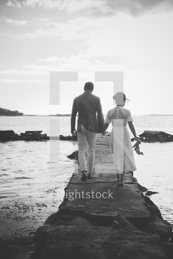 a couple walking on a jetty holding hands 