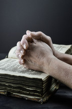 praying hands over an old worn Bible 