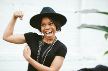 An African American woman in a black hat flexing her muscle 