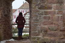 a woman looking out standing under a stone arch 