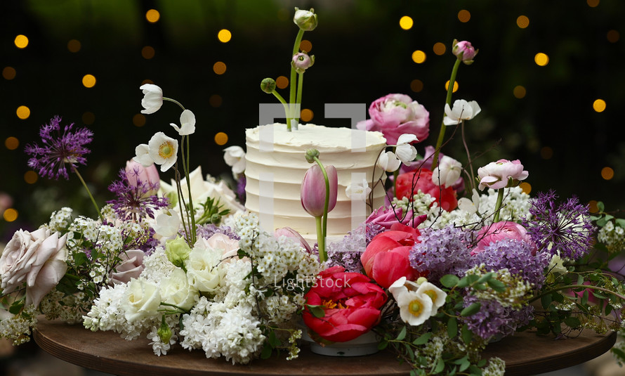 white wedding cake with fresh roses and wild flowers outdoors. Wedding decoration table in the garden, floral arrangement, In the style vintage. Wedding ceremony party.