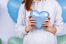 cropped photo of woman holding a blue balloon in the shape of a heart against her body on colorfull heart baloons background, close-up composition. Celebration for Valentine's Day.Romantic atmosphere