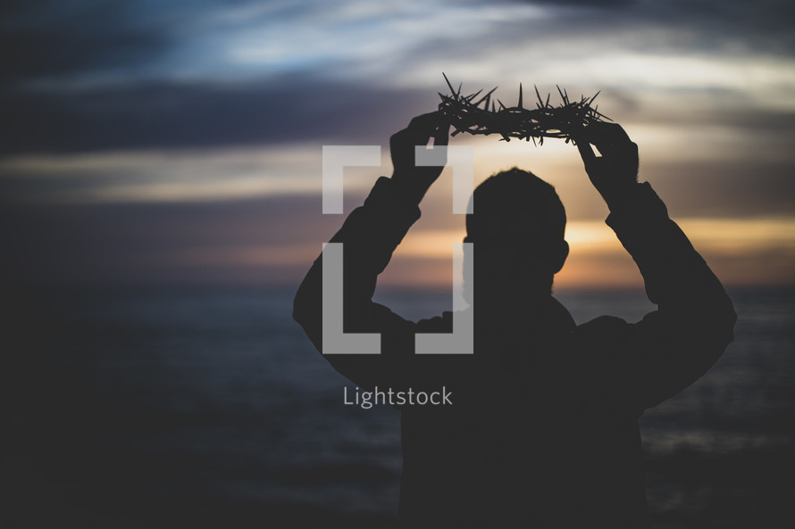 person holding up a crown of thorns at sunset 