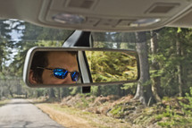 reflection of a man in sunglasses in a rearview mirror