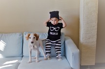 a toddler boy and dog standing on a couch 