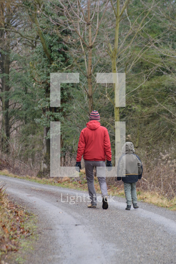 a man and a child walking together on a path through a forest 