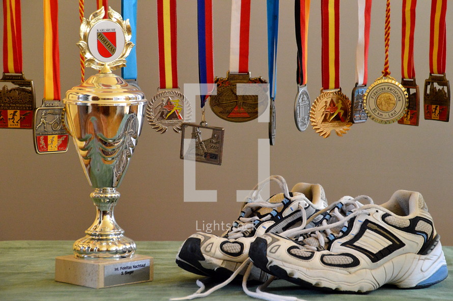 A pair of running shoes next to a trophy and medals.