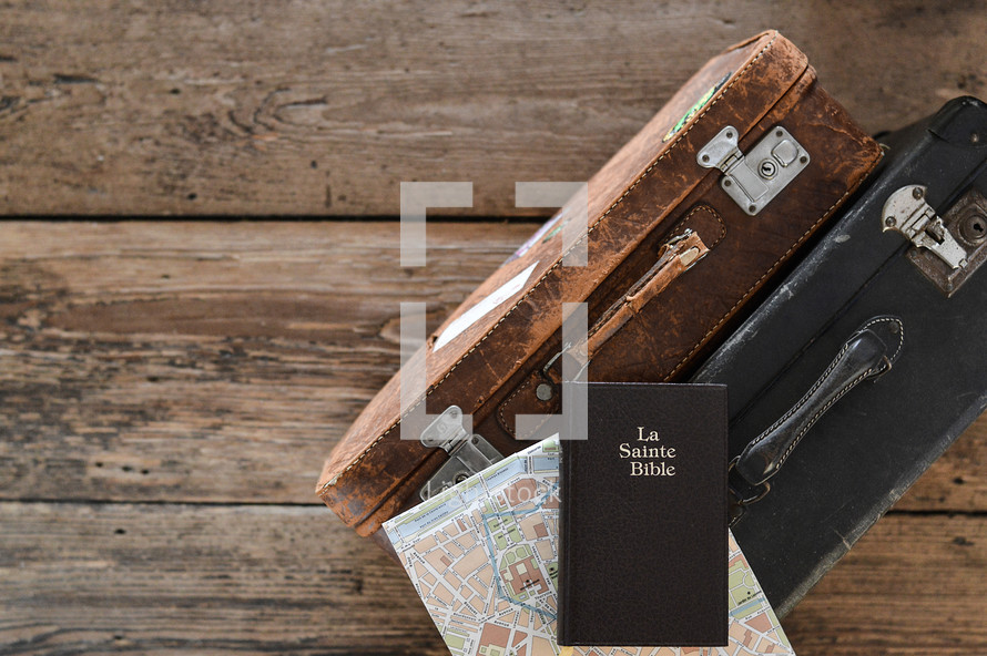 La Sainte Bible on luggage - two old weathered suitcases with a map of Paris and a french bible on a rustic wooden floor
