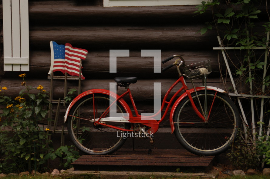 An American flag and red bicycle leaning against a log building.