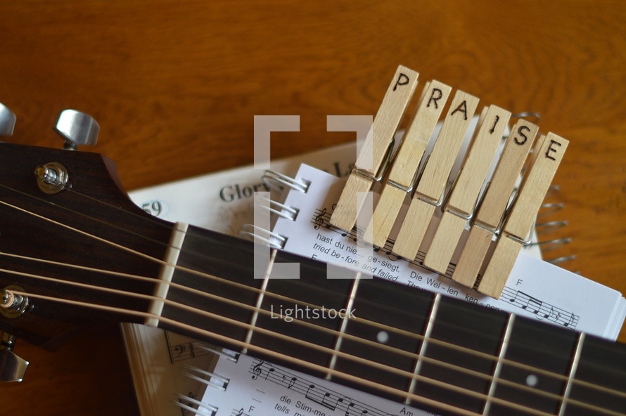 part of a guitar with the letters PRAISE burned into wooden clothespins and sheets of music. 