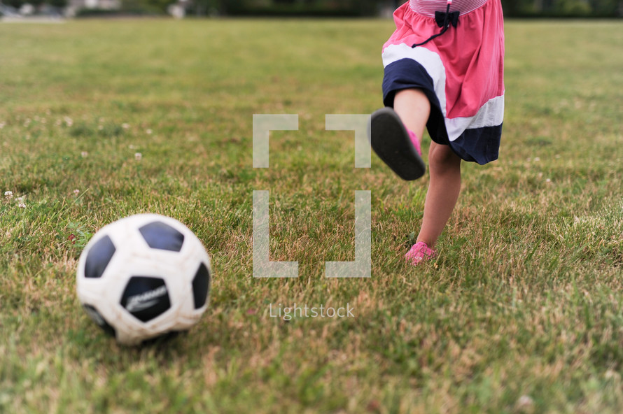a little girl in a dress kicking a soccer ball 