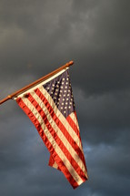 american flag hoisted up on flagpole in front of dark rainy cloudy sky while a storm is brewing
