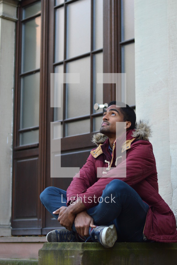 man sitting on steps in front of a church looking up 