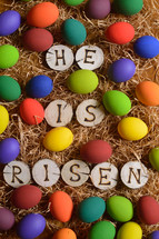 the words: HE HAS RISEN burned in wooden slieces between colorful painted eggs in straw 
