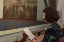 a woman reading a Bible sitting in a church alone 