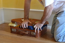 man trying to close his overstuffed suitcase