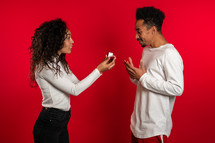African woman makes marriage proposal to her lover man with ring on red studio background.