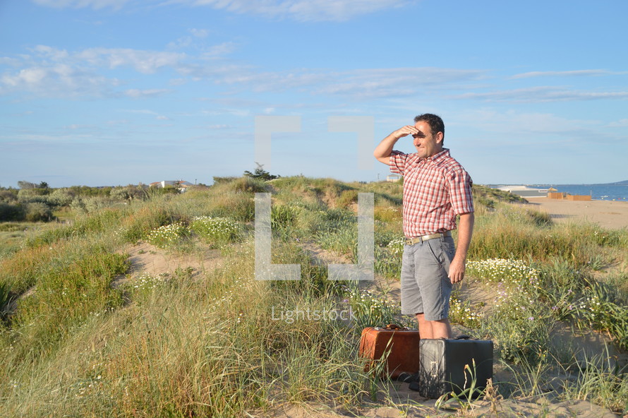 a man with luggage standing alone on sand dunes 
