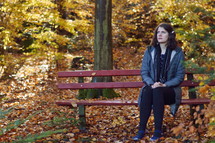 a woman praying on a bench in a park in fall 