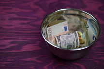 various currency in a bowl on a purple wood background 