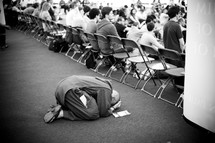 Person kneeling to the ground in prayer during a conference.
