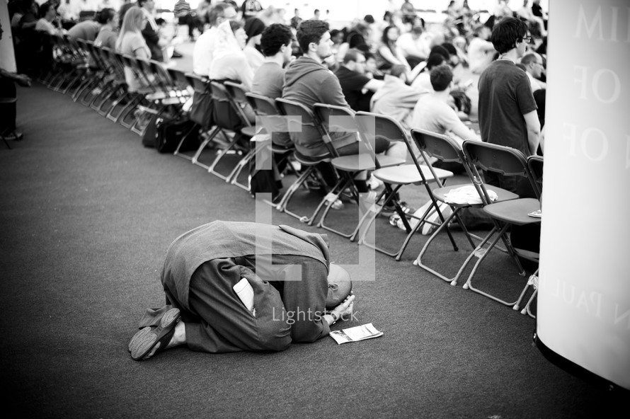 Person kneeling to the ground in prayer during a conference.