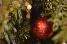 The Nativity story written in golden letters on a red Christmas ornament bulb hanging in a Christmas tree. 