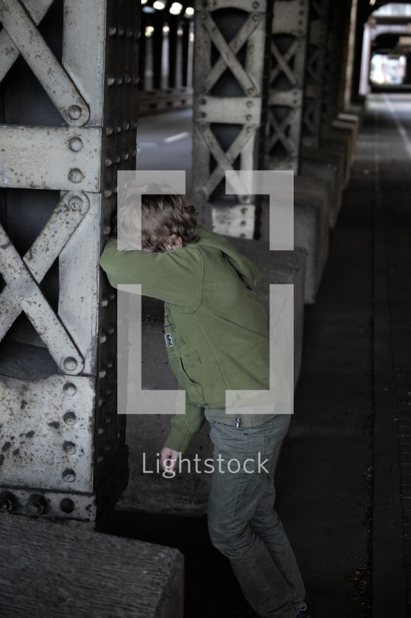a scared and lost little boy standing at a steel upright in a dark underground covering his face