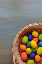 Colorfully painted Easter eggs on straw in a basket on a wooden table