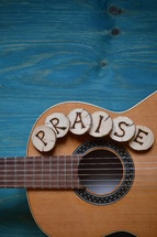 guitar on teal wooden background with wood pieces on it lettering the word: PRAISE