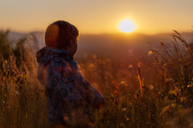 Boy looking towards the setting sun in a grassfield