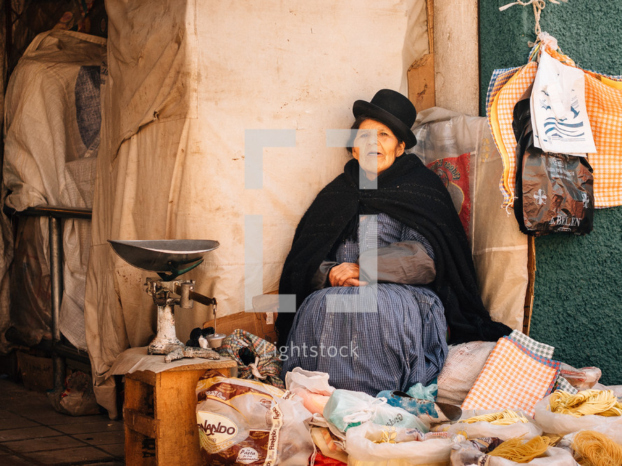 Woman in a hat sitting at an outside produce market.