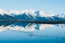 A snow capped mountain range reflected in a placid lake.