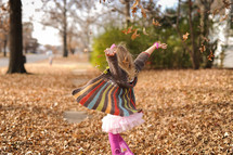 a toddler girl tossing fall leaves into the air 