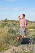 a man with luggage standing alone on sand dunes 