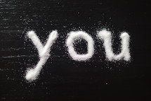 The word, "you," written in salt on a table.