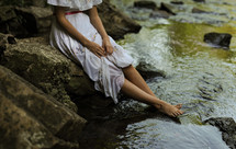 a woman in a dress sitting with her feet in the water 
