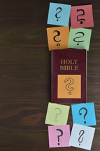 Holy bible and note pads with question marks on brown wood