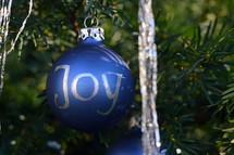 The words Joy, Love, Peace, Grace and Hope written in silver letters on blue Christmas ornament bulbs. 
