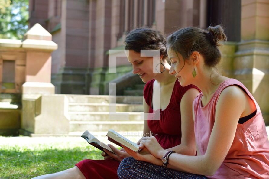 women reading Bibles together outdoors next to a cathedral