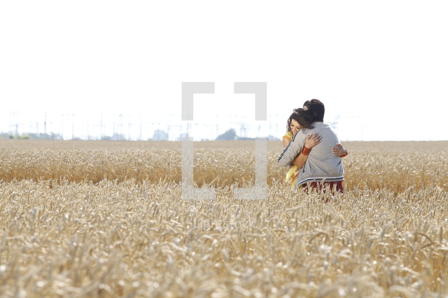 A man and woman embracing in a field of grain.