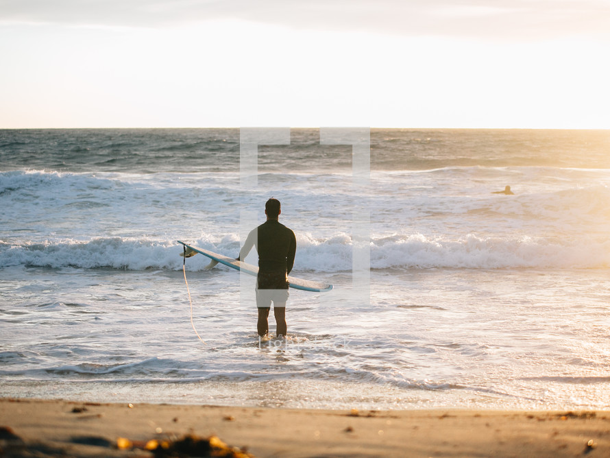 man with a surfboard standing in the ocean 
