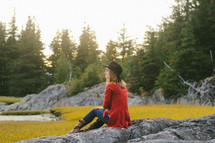 a portrait of a woman in a red sweater sitting on a rock 